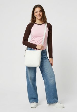 Young woman wearing pink and brown long-sleeve shirt, blue wide-leg jeans, white sneakers, and carrying a white shoulder bag.