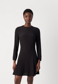 Melnas kleitas ar garām piedurknēm, apaļu kakla izgriezumu un paplatinātu svārku. Uz krūtīm ir neliela zīmola akcenta detaļa. Gluda, viegla auduma.