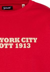 T-shirt di cotone rosso con collo girocollo a costine, caratterizzata da una scritta bianca audace: "NEW YORK CITY SCHOTT 1913" in un font in stile retro.