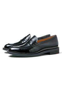 Schwarze Lederloafer mit glatter Oberfläche und dekorativer Naht. Rundliche Spitze und flacher Absatz mit einem kontrastierenden roten Akzent an der Sohle.