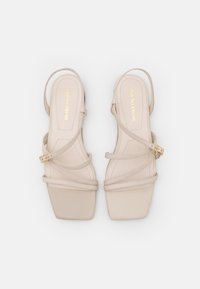 Beige sandaalit, joissa on suorakulmainen kärki, sileät nahkahihnat ja kultainen solki. Litteä pohja ja minimaalinen muotoilu.