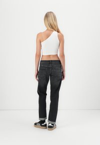 Mustad denim püksid, millel on vabalt istuv lõige, tagakotid ja volditud äär, koos valge ühe õlavarrega lühikese toppiga. Sneakerid on kaasas.