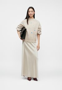 Beige sweater with blue heart patterns, cream satin maxi skirt, black handbag, and maroon pointed heels. Smooth textures and relaxed fit.