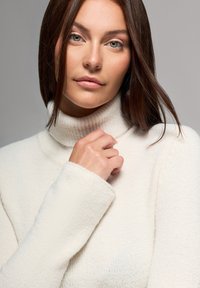 Biały dzianinowy sweter z golfem, z prążkowanym kołnierzem i szerokimi mankietami, z miękkiej, teksturowanej tkaniny i luźnym krojem.