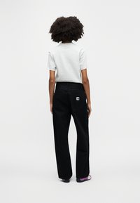 Γκρι πουκάμισο με κοντά μανίκια συνδυασμένο με ψηλόμεσα μαύρα τζιν που διαθέτουν λογότυπο στην πίσω τσέπη και φαρδιά γραμμή. Τα παπούτσια είναι σκουρόχρωμα με μωβ λεπτομέρειες.