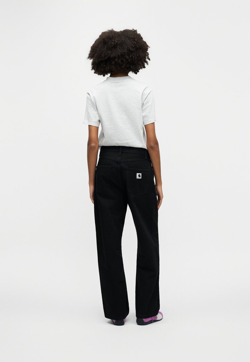 Grijs shirt met korte mouwen gecombineerd met hooggetailleerde zwarte spijkerbroek met een achterkantlogo op de zak en een wijde pijp. De schoenen zijn donker met paarse accenten.