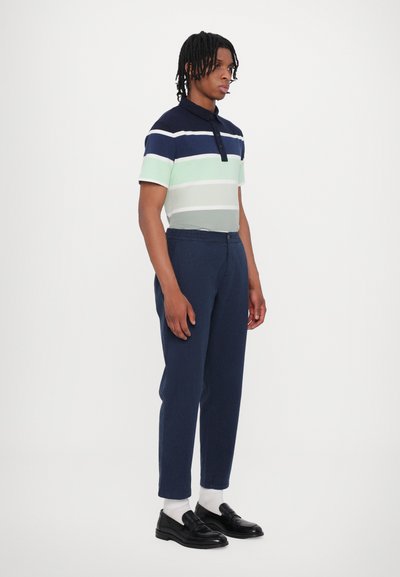 Polo skjorte med marineblå, grønn og hvit horisontale striper, korte ermer og krage. Kombinert med marineblå bukser og svarte loafers.