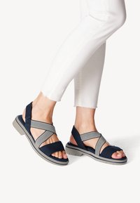 Navy blue sandals with crisscross elastic straps, a padded sole, and a textured gray outsole. Open-toe design reveals toes and nails.