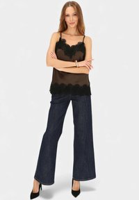 Czarna satynowa koszulka na ramiączkach wykończona czipką, zestawiona z szerokimi spodniami dżinsowymi o ciemnym odcieniu i czarnymi szpilkami z noskiem w szpic.