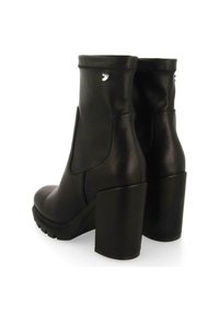 Botas de tobillo de cuero negro con un alto tacón de bloque, paneles laterales elásticos y un detalle del logo en el tacón. Textura suave con un diseño elegante.