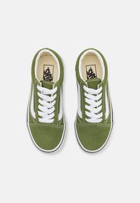 Sneakers in tela verde con lacci bianchi, striscia laterale e suola in gomma. La texture è liscia con cuciture a contrasto e un logo sulla soletta.