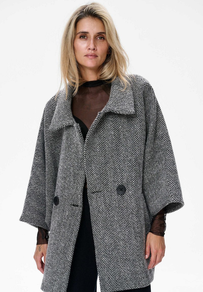 Grijs visgraat coat met brede mouwen, grote kraag en twee zwarte knopen, met een gestructureerde stof en een relaxte pasvorm.