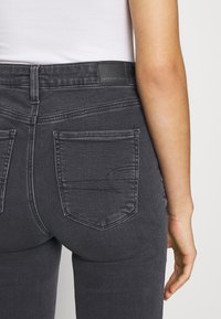 Dark gray denim skinny jeans with a mid-rise waistband, featuring two back pockets and a textured, soft finish. Label at the waistband.