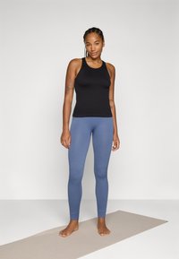 Svart ermeløs topp kombinert med blå ribbede leggings. Toppen har en tettsittende design; leggingsene sitter godt og er smale ved anklene.