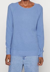 Pull en tricot bleu clair avec un motif texturé, encolure arrondie et poignets côtelés, associé à un jean bleu clair.