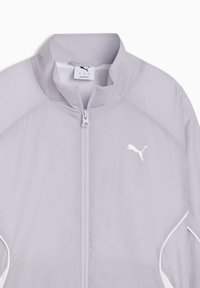 Ανοιχτό γκρι μπουφάν Puma με πλήρες φερμουάρ μπροστά, ψηλό γιακά, λευκό λογότυπο Puma στο στήθος και λευκές διακοσμητικές ρίγες στις πλευρές.