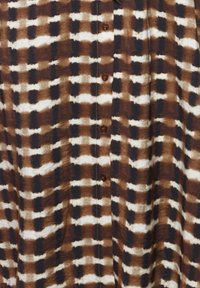 Tissu à carreaux marron, noir et blanc avec des boutons au centre, montrant une surface textile douce et texturée.