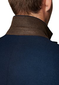 Granatowa tkanina kurtki o teksturowanym wykończeniu, z brązowym filcowym kołnierzem. Kołnierz ma gładką krawędź, co dodaje kontrastu wizualnego.