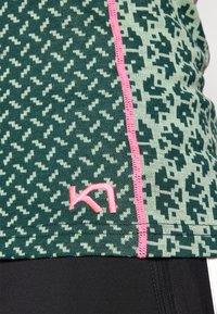 Grønt og lysegrønt mønstret treningsgenser med rosa sømmer og en rosa logo, laget av et elastisk, teksturert stoff. Svart base under.