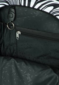 Interno nero di una borsa con una tasca con zip e un motivo circolare. Il materiale è testurizzato con un leggero branding su uno sfondo scuro.