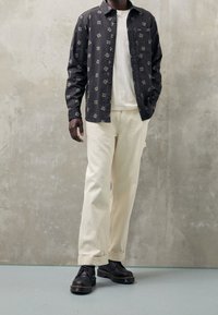 Zwart overhemd met bloemenpatroon, wit T-shirt, creme wijde broekspijpen en zwarte schoenen met dikke zolen. Gladde textuur, casual ontwerp.