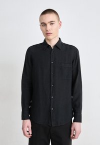 Camicia nera a maniche lunghe in tessuto leggero, caratterizzata da un design con bottoni, colletto e taschino sul petto. Taglio con orlo curvo.