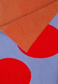 Tkanina z niebieskim tłem i dużymi czerwonymi okręgami, nałożona na wzorzystą pomarańczową tkaninę. Obie warstwy mają gładką teksturę.