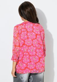 Przezroczysta różowa bluzka z kwiatowym wzorem i serduszkami, rękawy do łokcia z falbanami oraz luźny krój.