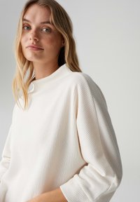 Lichtgewicht geribbelde coltrui in wit. Heeft een hoge halslijn en een ontspannen pasvorm met driekwartmouwen en gestructureerde stof.