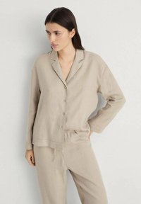 Beige loungewear set made of linen; features a button-up shirt with a collar and long sleeves, paired with elastic-waist trousers.