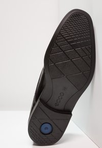 Semelle de chaussure en caoutchouc noir avec un motif d'adhérence texturé, un accent circulaire bleu, et le logo "ecco". Vue en angle montrant la semelle sur un fond clair.