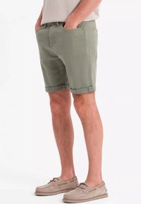 Shorts en coton vert clair avec un ourlet roulé, dotés de poches latérales et d'une texture lisse. Complétés par des chaussures de style mocassin couleur beige clair.