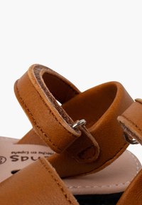 Sandali in pelle marrone con due cinghie regolabili e accessori in argento, dotati di una suola interna testurizzata e di una soletta liscia color beige.