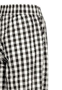 Pantalon en tissu à carreaux noir et blanc avec une ceinture élastique et une poche latérale, montré depuis la zone des hanches.