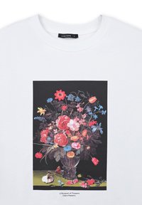 T-shirt bianco con una stampa dettagliata di un vivace bouquet floreale in un vaso, con fiori misti rossi, blu, gialli e rosa su uno sfondo nero.