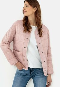 Lys pink quiltet jakke med rund halsudskæring, trykknaplukninger og sidelommer, båret over en hvid T-shirt og blå jeans.