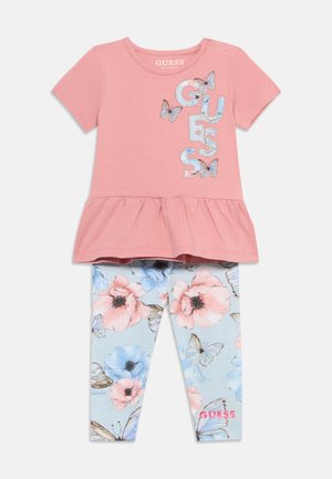 Rosa Kurzarmoberteil mit "GUESS"-Schriftzug und Schmetterlingsdruck, kombiniert mit hellblauen Leggings mit rosa und blauen Blumen sowie Schmetterlingen.