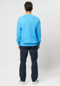 Jersey azul claro de manga larga con puños y cuello acanalados. Combinado con pantalones azul marino oscuro. Se ven zapatos con suela de goma en la parte inferior.