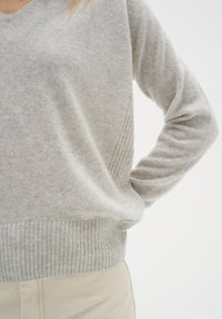 Ljusgrå tröja med V-ringning, ribbad nederkant och texturerade sidodetaljer. Tillverkad av mjukt material, har en avslappnad passform och långa ärmar.