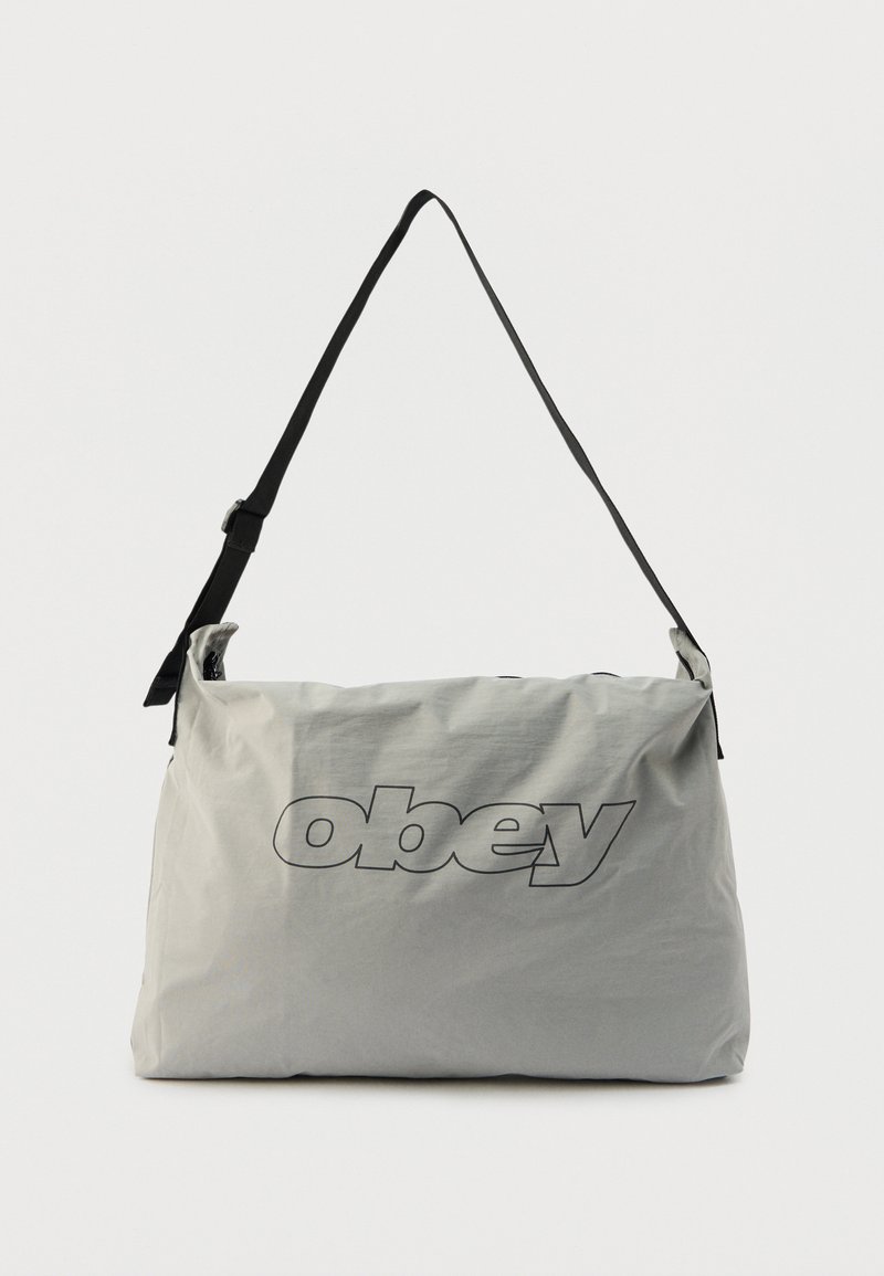 Ανοιχτό γκρι τσάντα ώμου με ρυθμιζόμενο μαύρο λουρί, διακοσμημένη με μεγάλο περίγραμμα λογότυπο "obey" στο κέντρο του μπροστινού μέρους.
