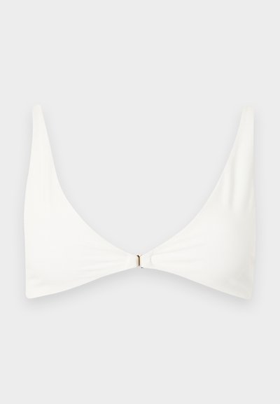 Λευκό μινιμαλιστικό τοπ μπικίνι με λεπτές τιράντες στους ώμους και μικρό χρυσό κούμπωμα στο κέντρο μπροστά, σε απλό ανοιχτό φόντο.