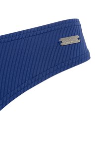 Námornícky modrý bandeau top s vertikálnou ribbovou textúrou, s kovovým štítkom v striebornej farbe označeným "Venice Beach" a kontrastným prešívaním.