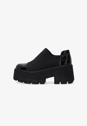 Black platform shoe with chunky lug sole, shiny patent toe cap and heel, and smooth fabric upper.