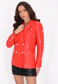 Blazer roșu din ecopiele cu embellishments asemănătoare cu perlele, design cu dublu breasted, rever în formă de cuțit și buzunare laterale. Stilizat cu o fustă mini neagră.