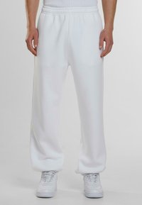 Witte sweatpants gemaakt van zachte, gladde stof met een elastische tailleband en zijzakken, gecombineerd met witte sneakers.