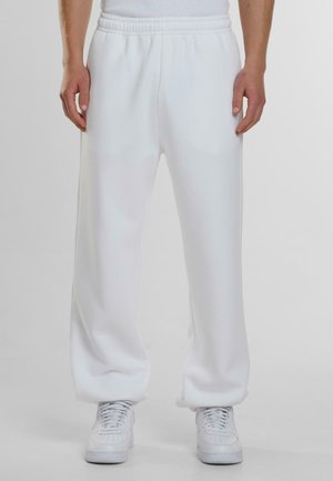 White sweatpants made from soft, smooth fabric with an elastic waistband and side pockets, paired with white sneakers.
