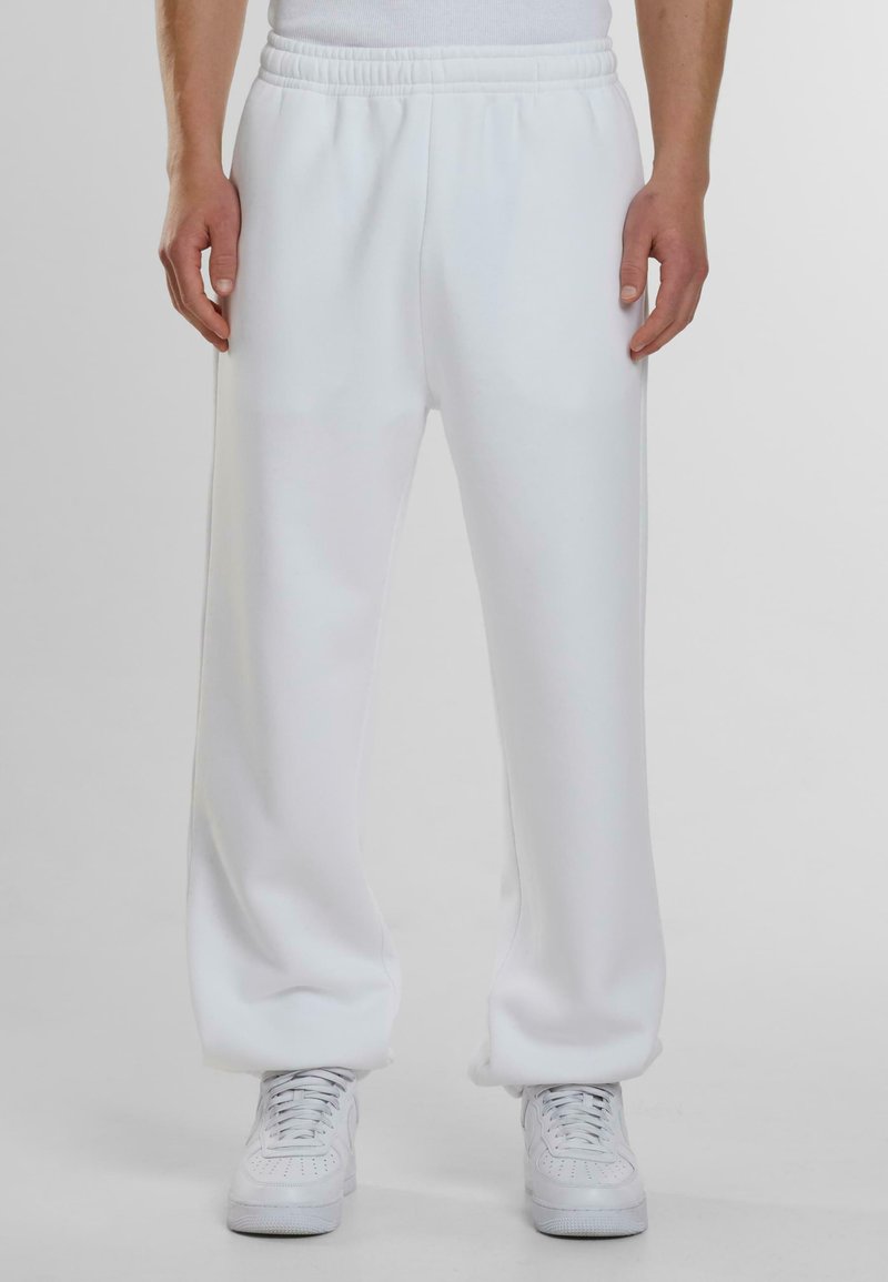 Witte sweatpants gemaakt van zachte, gladde stof met een elastische tailleband en zijzakken, gecombineerd met witte sneakers.