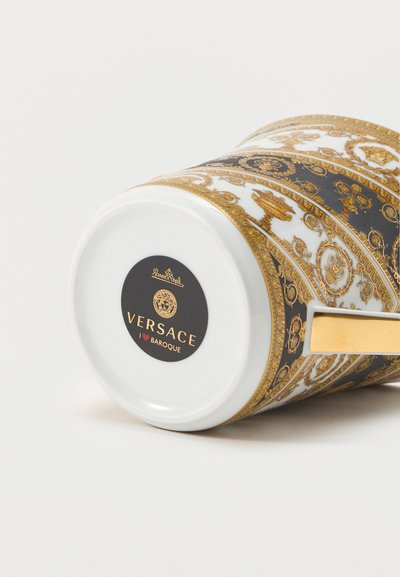Λευκός πορσελάνινος φλιτζάνι Versace Baroque με περίπλοκα χρυσά και μαύρα μπαρόκ σχέδια και χρυσή λαβή, απεικονισμένο σε οριζόντια θέση.