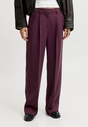 Pantalon droit couleur prune porté avec des chaussures noires et une veste courte en cuir noir par-dessus un haut blanc.