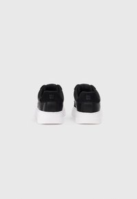 Black sneakers with a smooth leather upper, white rubber sole, and textured accents. Features branding on the heel and a padded collar.